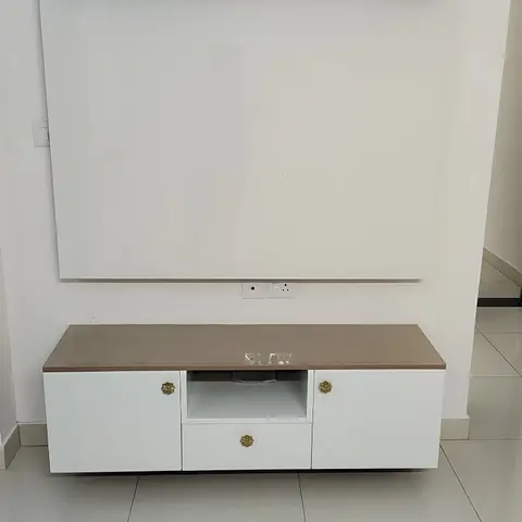 Freshly installed white TV feature wall with a wood-edge floating shelf above and a floating white console with brass floral knobs below.