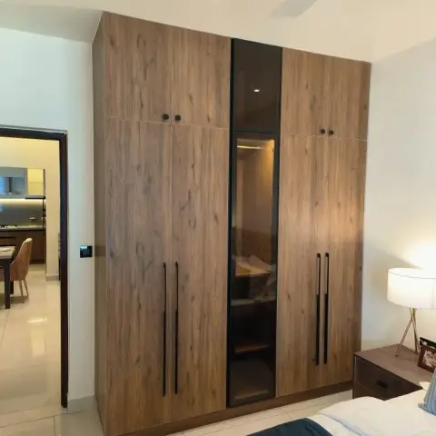 Full-height dark-oak laminate wardrobe with separate lofts and long matt-black bar handles, a smoked-mirror centre shutter in a black frame