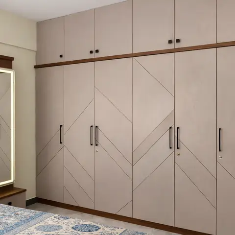 Full-length chevron-pattern wardrobe wall with dark wood trim beside a backlit LED full-height mirror, corner of a floral-linen bed visible.