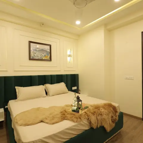 Full-wall emerald channel-tufted headboard running past the bed to a floating white side ledge, under ivory moulding frames with brass-and-marble linear sconces