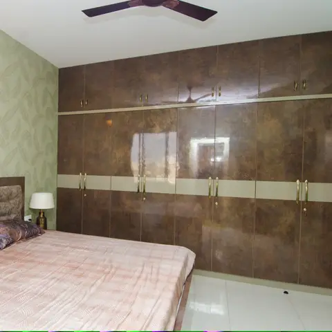 Full wall of bronze high-gloss wardrobes with lofts above, split by a cream horizontal band and antique-brass handles