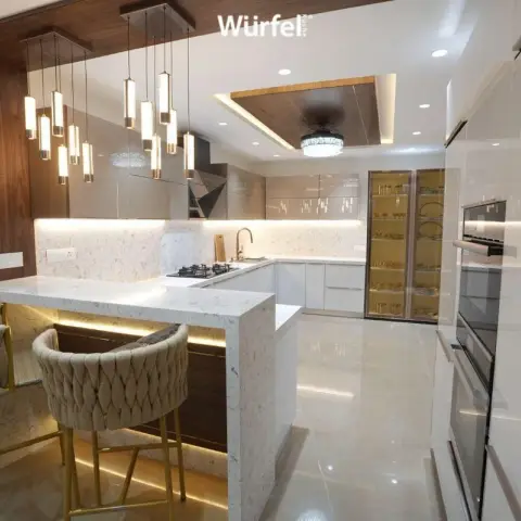 G-shaped ivory gloss kitchen with a veined quartz breakfast peninsula lit from underneath, a staggered row of gold-banded cylinder pendants