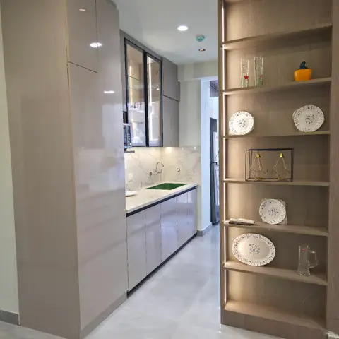 Galley kitchen in glossy taupe cabinetry with marble backsplash, opening onto a lit open crockery display shelf styled with plates and glassware.