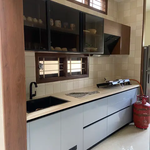 Galley kitchen mid-use with grey glossy lower shutters, a black granite-effect sink and a portable two-burner stove connected to an LPG cylinder.