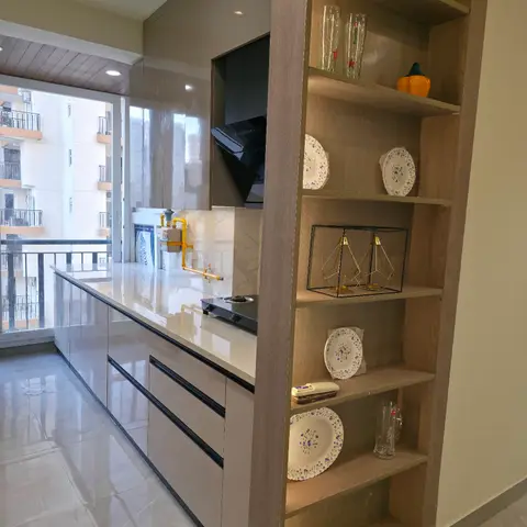Galley kitchen with glossy taupe cabinets and marble-effect backsplash, divided from the corridor by an open shelving unit styled with plates and glassware.