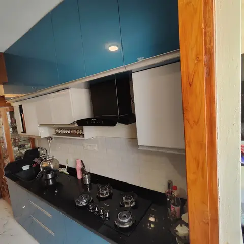 Galley kitchen with glossy teal upper and lower cabinets, a black granite counter and four-burner hob below a wall chimney, white subway-tile backsplash