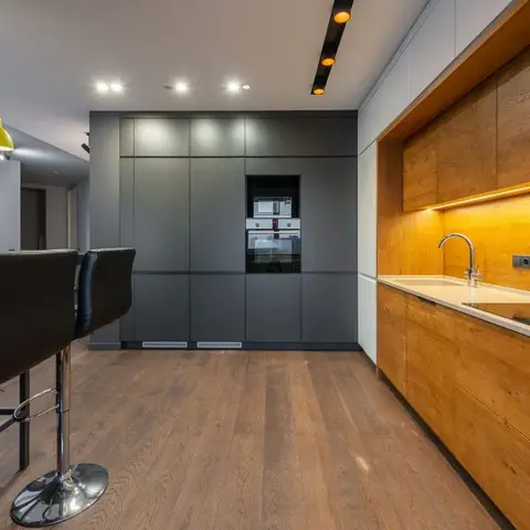 Galley kitchen with warm wood-grain handleless cabinetry and under-cabinet lighting along one wall
