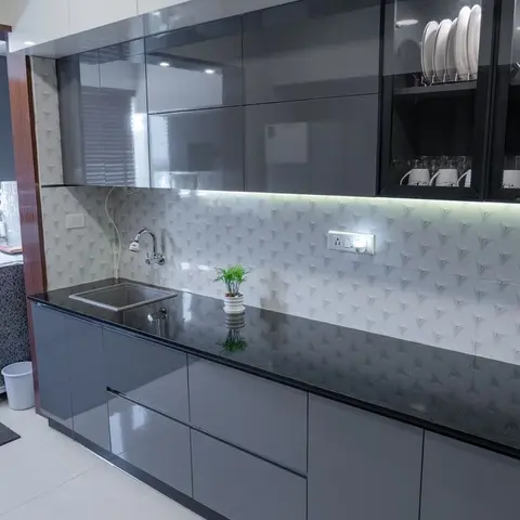 Galley modular kitchen with grey high-gloss shutters, a black granite counter, and a 3D textured tile backsplash lit by profile lighting.
