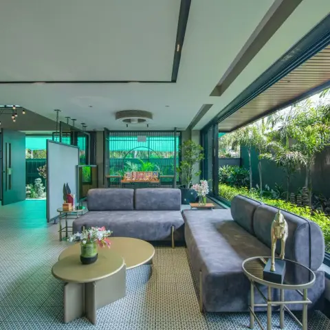 Garden-facing lounge where grey suede low-back sofas line full-height glazing, brass kidney nesting tables sit on a small-scale mosaic floor