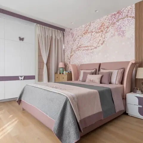 Girl's bedroom with a cherry-blossom mural wallpaper headboard wall, pink upholstered bed and a butterfly-appliqued white wardrobe.