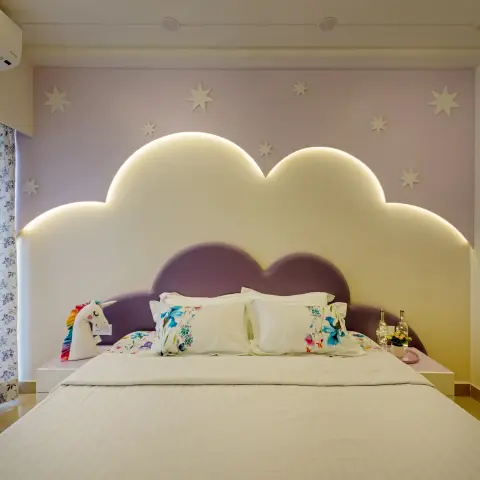 Girl's bedroom with a cloud-shaped upholstered headboard lit with a warm LED backlight and 3D star wall decor against a lilac accent wall