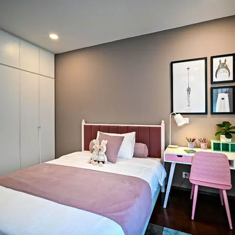 Girl's bedroom with a mauve upholstered headboard bed, a floor-to-ceiling white wardrobe wall and a pink study desk with a gallery of framed prints
