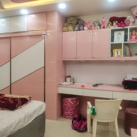 Girl's bedroom with a pink-and-white diagonal color-block glossy wardrobe and a matching built-in study desk topped with stuffed toys and cubby shelves.