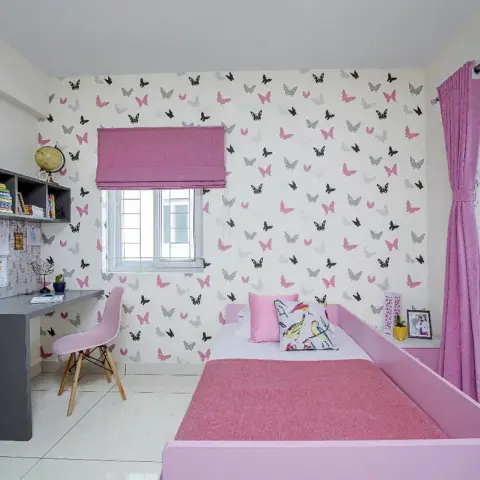 Girl's room with a pink-and-black butterfly wallpaper wall, a wall-hung grey study desk carrying a pinboard of crayon drawings and a globe