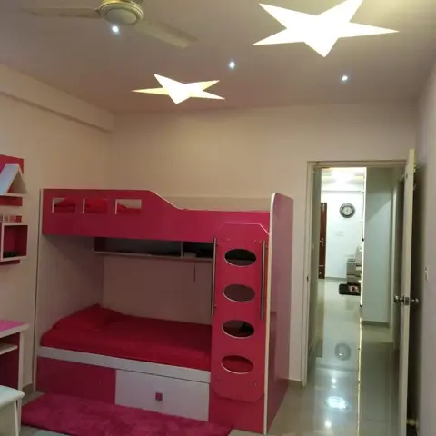 Girls' kids bedroom with a pink bunk bed with slide-out drawer, star-cutout ceiling with cove lighting, and a matching pink study desk.
