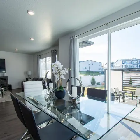 Glass-top dining table with black leather chairs and a mirrored candle-holder centerpiece, opening through sliding doors to a patio