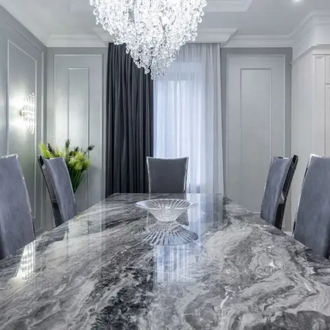 Grand dining table with a bookmatched grey marble top and velvet high-back chairs beneath an oversized crystal chandelier.