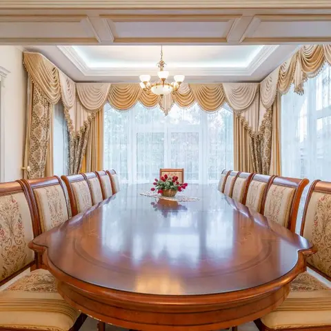Grand formal dining room with a long oval carved-wood table seating twelve upholstered chairs beneath a crystal chandelier and ornate swag curtains