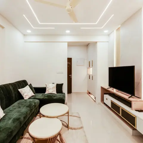 Green velvet L-shaped sofa facing a floating gold-trimmed TV console under a cove-lit ceiling with a marble-look fluted feature wall.