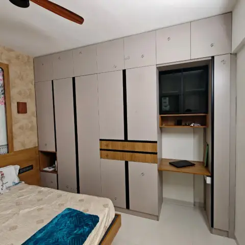 Greige wardrobe run banded with black grooves and teak strips, wrapping into a built-in study niche with a tinted-glass overhead unit