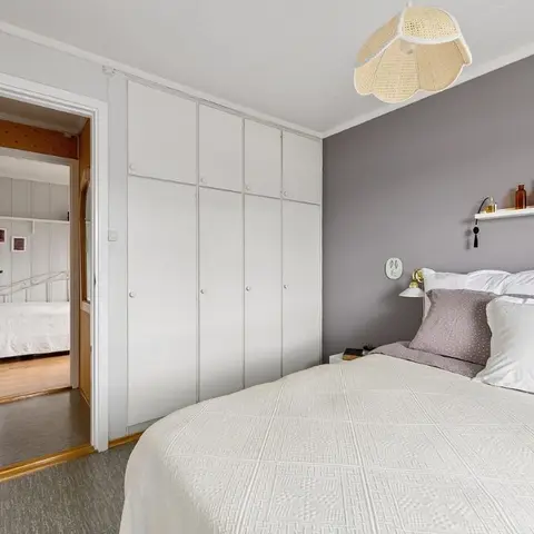 Grey-accent-wall bedroom with a scalloped rattan pendant, a slim white picture shelf of candles and bottles above the bed