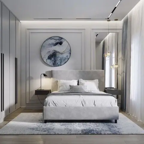 Grey-and-white bedroom where a round ink-wash abstract disc hangs inside a moulded wall frame over a velvet upholstered bed