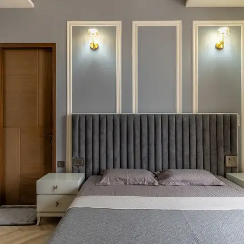 Grey bedroom with three white-framed wall panels above a full-width channel-tufted grey velvet headboard