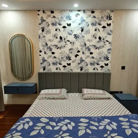 Grey channel-tufted headboard set against a blue watercolour-floral wallpaper panel framed by fluted beige battens