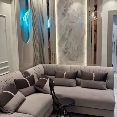 Grey channel-tufted L-shaped sofa with brown accent cushions in a living room with a book-matched marble feature wall flanked by fluted gold-lined panels and a