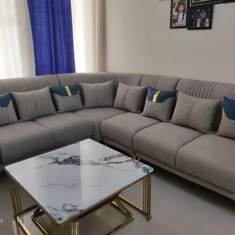 Grey channel-tufted L-shaped sofa with diamond-quilted and blue-and-gold accent cushions, a gold-framed marble-top coffee table