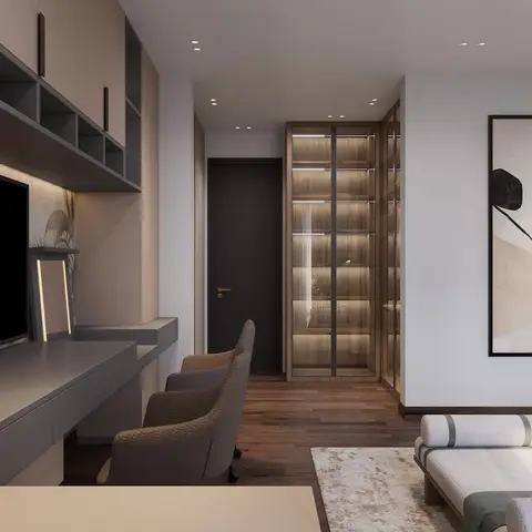 Grey desk-and-TV run with overhead open cubbies down one side of a bedroom, looking past a bouclé chair to a bronze-framed glass walk-in wardrobe lit shelf by