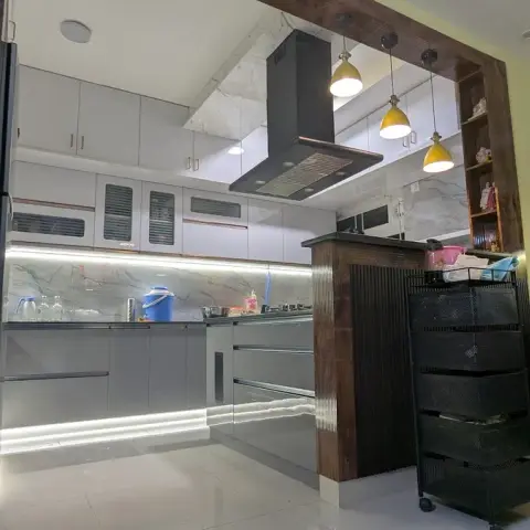 Grey-gloss kitchen with a fluted dark-wood breakfast peninsula, a black box chimney over the hob and three yellow dome pendants hung against a grey-veined