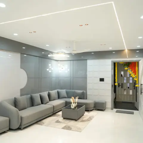 Grey high-gloss panelling with a curved cut-out behind a low L-sofa and wheeled ottomans, a mitred LED profile line tracing the white POP ceiling