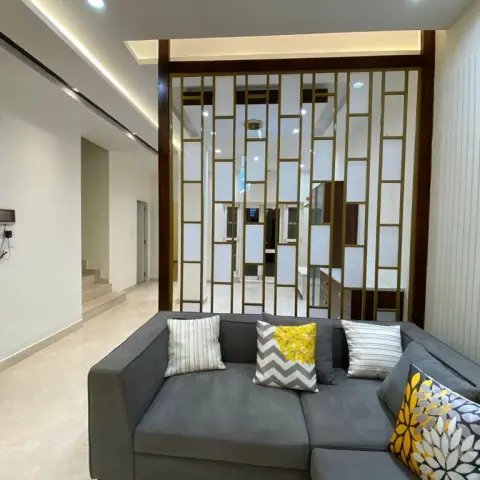 Grey L-shaped sofa with yellow-and-white patterned cushions set against a brass-framed frosted-glass grid partition