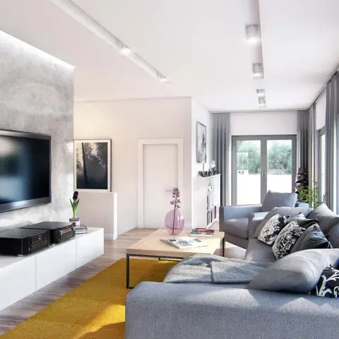 Grey microcement TV panel washed by a ceiling recess above a gloss-white floating media unit, with a grey sectional on a mustard rug facing full-height glazing.