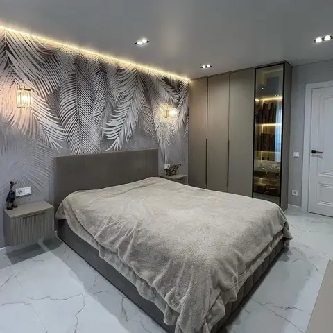 Grey palm-frond photo mural filling the headboard wall, grazed by a cove strip at the ceiling and punctuated by two brass crystal sconces