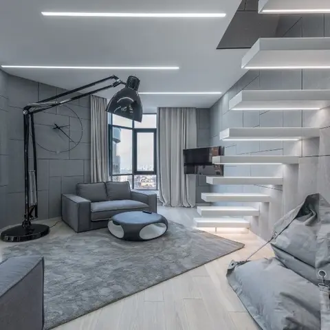 Grey panelled living room with a floating cantilevered staircase and an oversized articulated floor lamp beside a round marble coffee table.