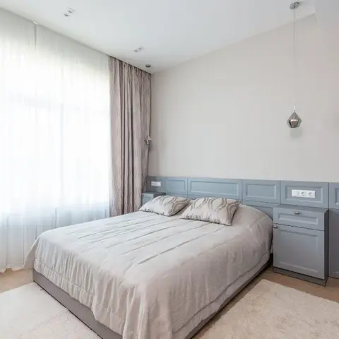Grey shaker-panelled dado runs behind the bed and turns into a bedside drawer and a desk with a mauve chair, lit by one faceted chrome pendant on a long cord.