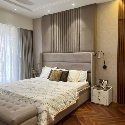 Grey suede headboard wall carried floor-to-ceiling with a channel-tufted centre panel, teak herringbone floor