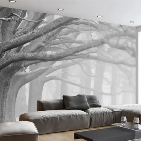 Grey-taupe modular sofa and a clear-acrylic coffee table set against a full-wall black-and-white mural of a spreading oak in fog.