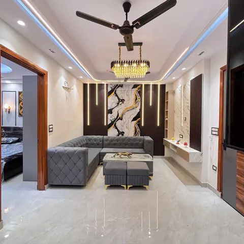 Grey tufted L-shaped sectional living room with a crystal chandelier under a blue-lit cove ceiling and a fluted dark-wood panel wall with marble-effect art.
