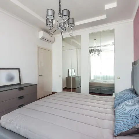 Grey upholstered bed against a dusty-rose head wall carrying two chrome swing sconces and a pair of botanical prints