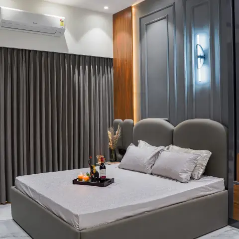 Grey upholstered storage bed with a three-arch padded headboard against a charcoal moulded panel wall lit by a chrome LED sconce