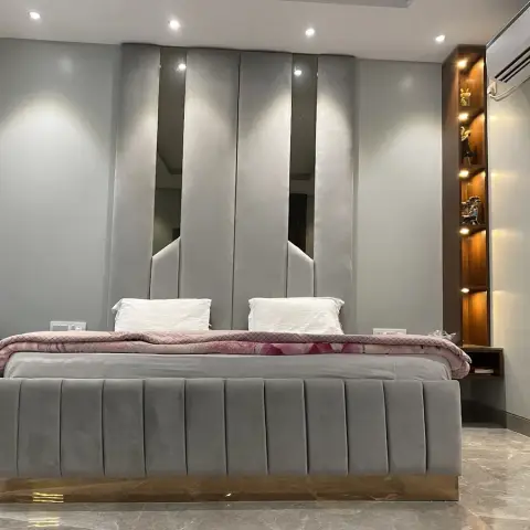 Grey velvet channel-tufted bed on a brass plinth against tall upholstered wall panels separated by mirror slivers