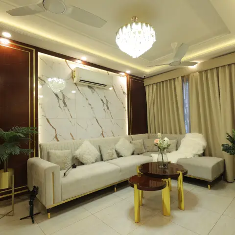 Grey velvet corner sofa with gold trim facing a backlit marble slab feature wall framed by dark wood and gold-inlay panelling