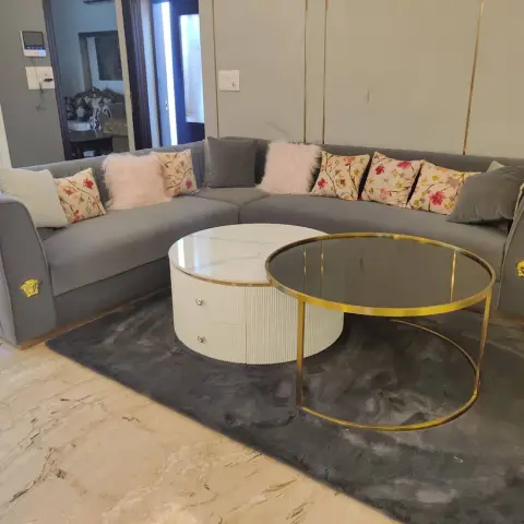 Grey velvet corner sofa with gold medallion studs on its arms and a bank of floral and blush-fur cushions