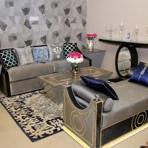 Grey velvet sofa piled with embroidered and navy cushions beside a gold-trimmed velvet chaise with crystal finials, around a brass-inlay coffee table
