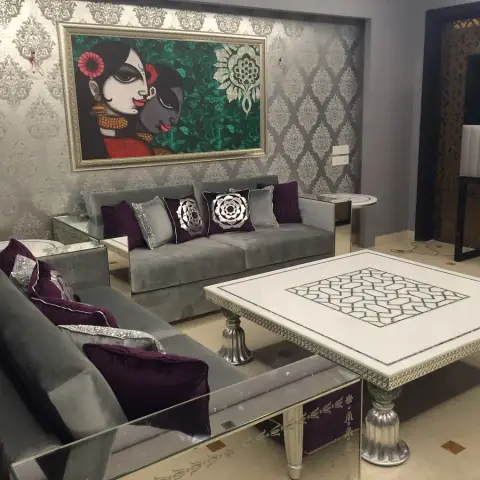 Grey velvet sofas with aubergine and sequinned silver cushions set against silver damask wallpaper, under a framed Radha-Krishna painting