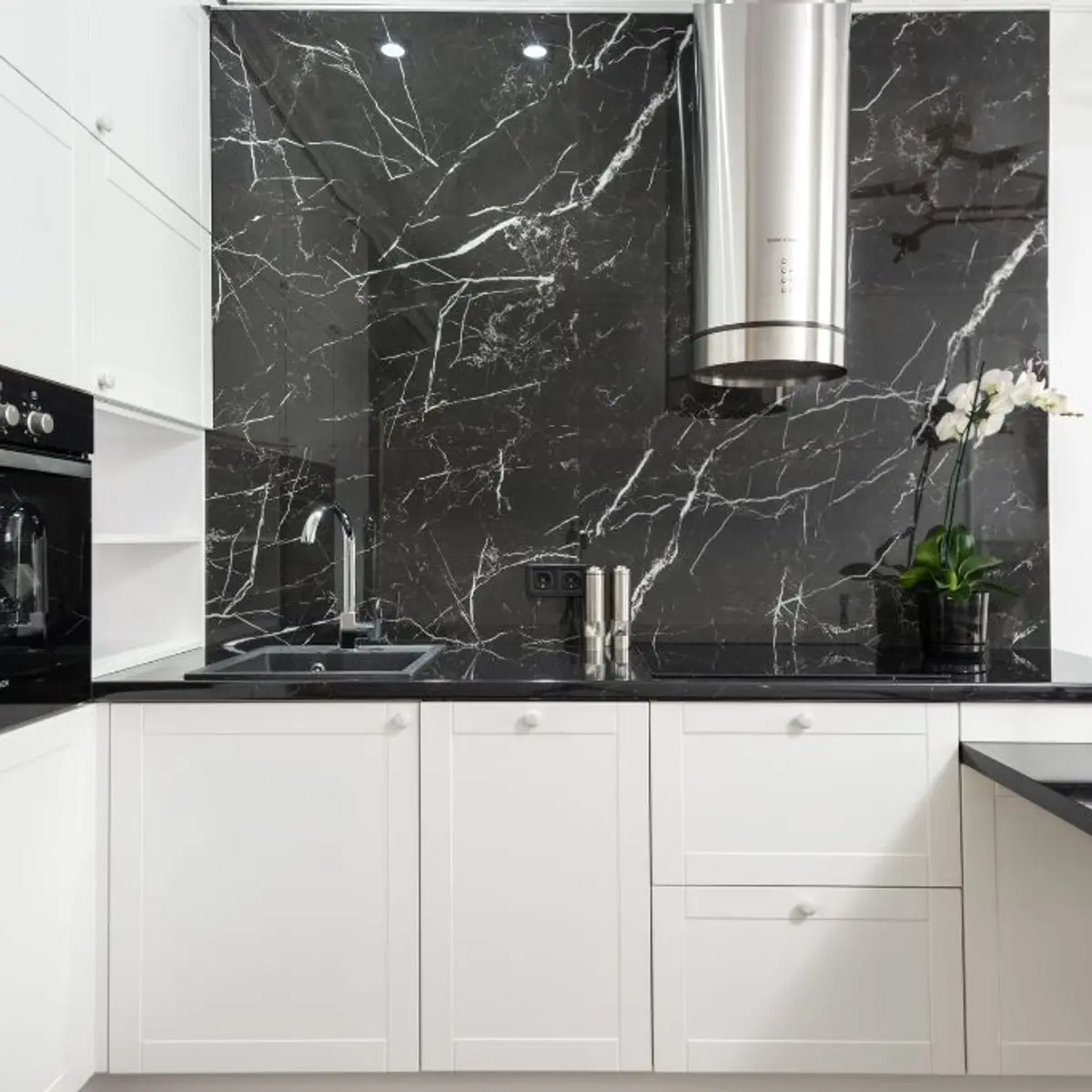 White shaker kitchen with veined marble slab backsplash and cylindrical chimney hood