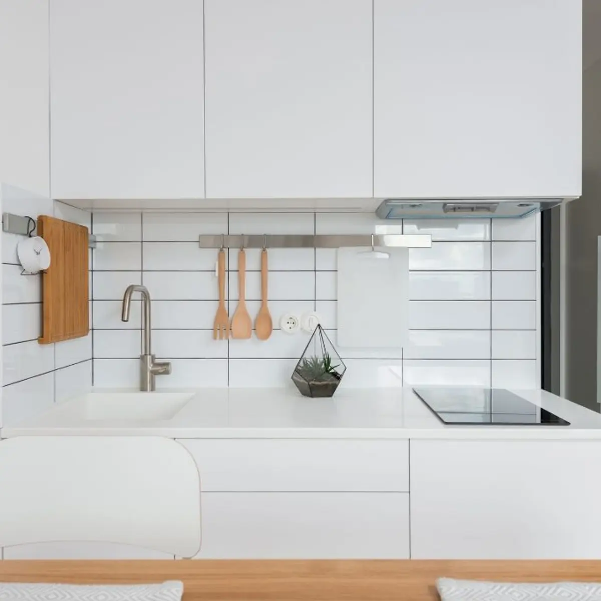Compact all-white kitchenette with grid tile backsplash and utensil rail